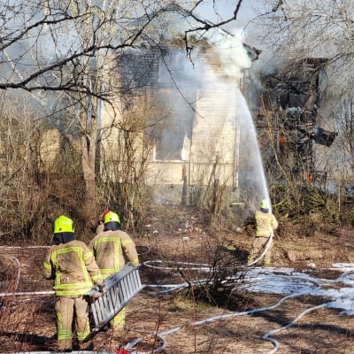 Brandmän som bär en stege mot ett brinnande hus. 