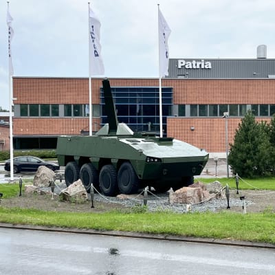 Patrian tehdasalueen sisäänkäynnin edustaa Hämeenlinnssa. Päärakennuksen edessä on kahdeksanpyöräinen panssariajoneuvo, sen takana kolme Patrian lippusalkoa.