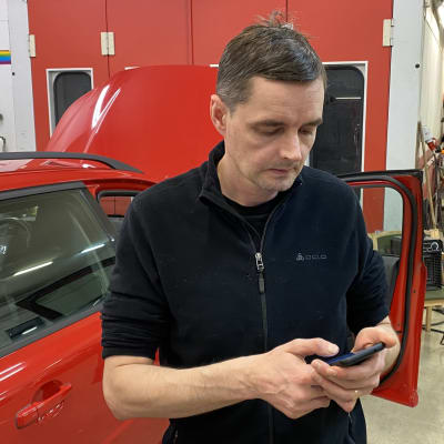 Mies katsoo kännykkäänsä autokorjaamon tiloissa.