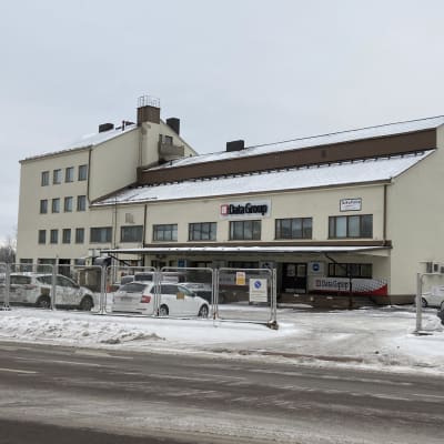 Valkoinen kivirakennus, jonka eteen on pysäköity autoja.