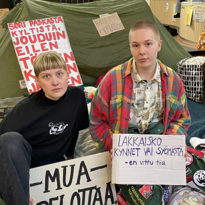 Lapin yliopiston opiskelijat  Aino Jäälinoja ja Kajo Pippuri istuvat yliopiston pääaulan lattialla mielenosoituksessa.