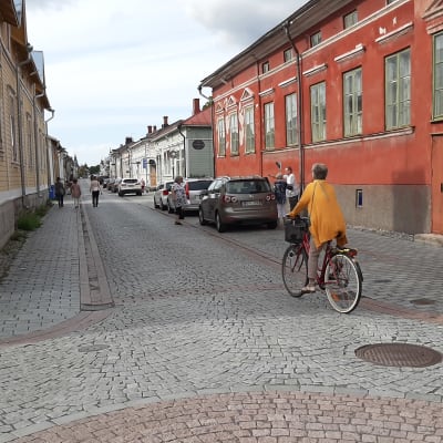 En cyklist med gul tröja cyklar på den stenlagda gatan mellan trähusen i Gamla Raumo.
