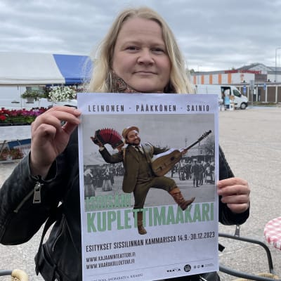 Nainen pitää teatterimainosta käsissään torin laidalla.
