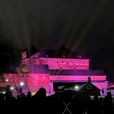Punaisessa valossa hohtava Hämeen linna uudenvuodenaaton illan valotulituksessa.