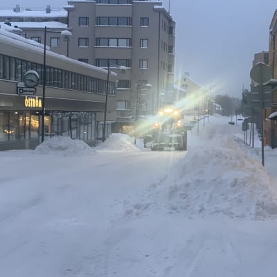 En fronlastare plogar snö i centrum av en liten stad. 