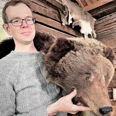 En man med glasögon håller en björnpäls över sin axel. 