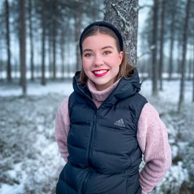 Riikka Karppinen nojaa puuhun ja hymyilee Viiankiaavan lumisella suolla alkutalvella 2021.