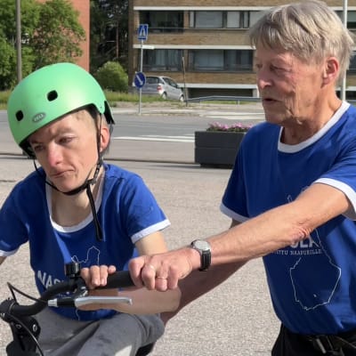 Kalevi Laaksonen auttaa kehitysvammaista Veikka-poikaansa pyöräilyssä. Veikalla kypärä päässään, isä pitää kiinni pyörästä.