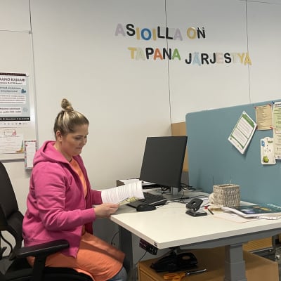 Jännittäjäryhmän ohjaaja selaa kirjaa työpisteellä, takana seinällä lukee teksti "asioilla on tapana järjestyä".
