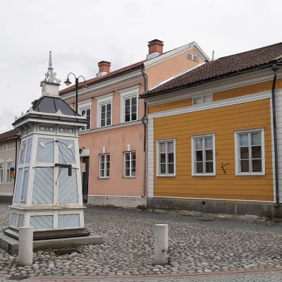 En ljusblå brunn står mitt på den stenlagda gatan mellan trähus i Gamla Raumo.
