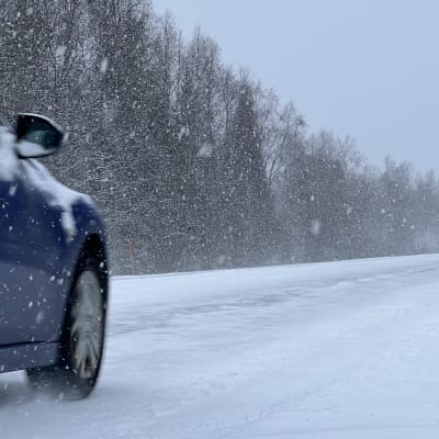 Henkilöauto ajaa lumisateessa lumisella tiellä lokakuussa 2022