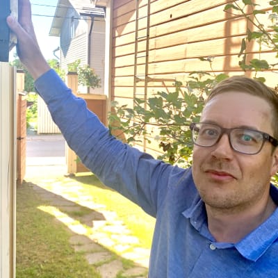 En man med glasögon står med handen mot en halvbyggd träfasad. 