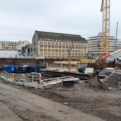 Byggkonstruktioner, ställningar, lastbilsflak och en byggkran står i gropen till det som byggs till en torgparkering under Salutorget i Åbo.
