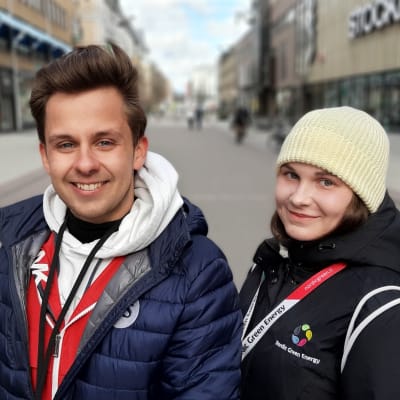 En ung man och en ung kvinna tittar in i kameran och ler. De står på en tom gågata.
