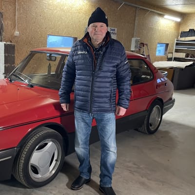 En man står i ett garage. Bredvid sig har han en röd Saab Turbo.
