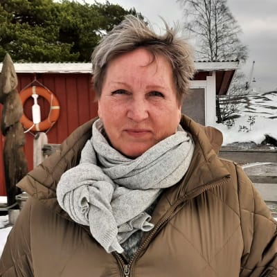 Kvinna framför röda sjöbodar vid havet.