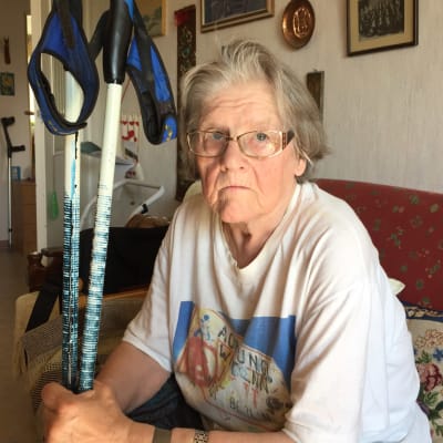 En äldre kvinna som sitter på en soffa och håller i ett par stavar.