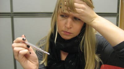 En kvinna håller sig för pannan och tittar på en febertermometer.