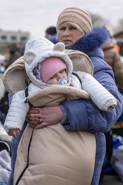 En kvinna håller i en bebis i famnen. Bredvid henne andra människor samlade.