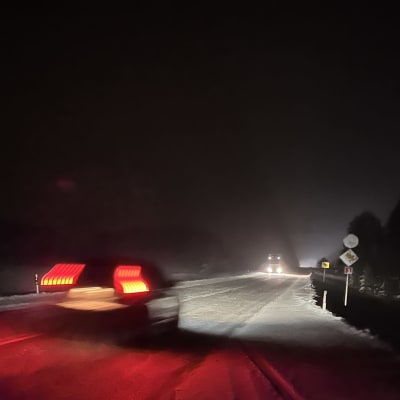 Auto ajaa valtatiellä lumisessa maisemassa ja vastaan tulee raskas ajoneuvo.