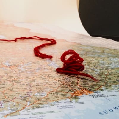 Finlands karta och ett frågetecken i röd ylletråd.