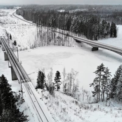 Lumisessa maisemassa jäätynyt joki, jonka ylittää kaksi siltaa. Kuvattu yläviistosta.
