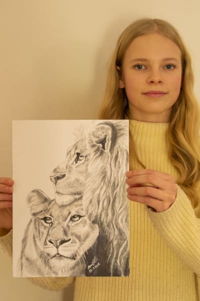 En ung tjej håller upp en teckning av två lejon, som hon själv har gjort.