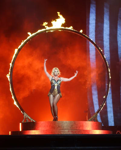 Britney Spears uppträder på en scen. Hon omgivs av en cirkel av stål som brinner.
