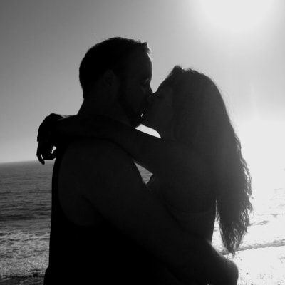 En man och en kvinna kysser varandra på en strand, svartvit