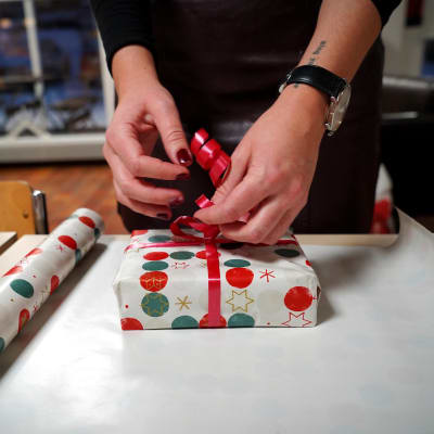 Händer som slår in ett paket i julpapper.