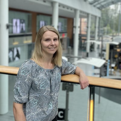 Nainen nojaa kauppakeskuksessa ylikulkusillan kaiteeseen.