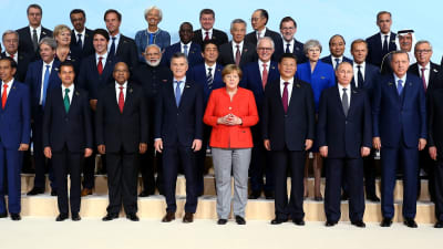 Gruppbild från G20 toppmötet i Hamburg, Angela Merkel i röd kavaj står bland andra en massa andra ledare som alla är klädde i svart eller mörkblått.