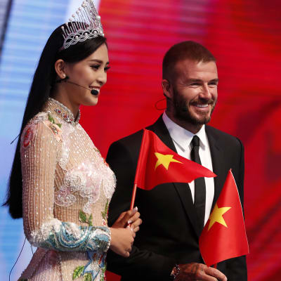 David Beckham och Miss Vietnam håller i varsin vietnamsflagga och står framför en stor vietnamflagga.