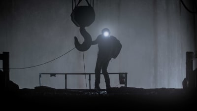 På bilden en man med pannlampa intill den vita väggen nere i gruvan.