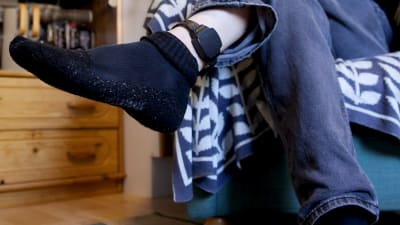 En person vars ansikte inte syns har lyft upp foten för att visa en elektronisk fotboja hen har runt fotleden