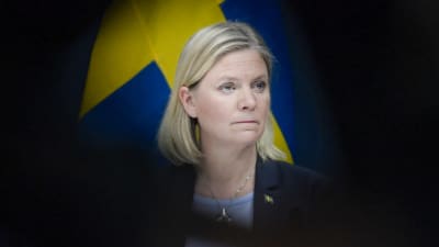 Magdalena Andersson tittar åt sidan. I bakgrunden syns Sveriges flagga.