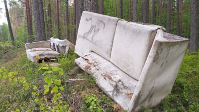 En vit soffa som lämnats i skogen.