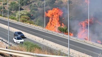 En stor markbrand härjar precis intill en motorväg där det kör två bilar 26 juli 2022. 