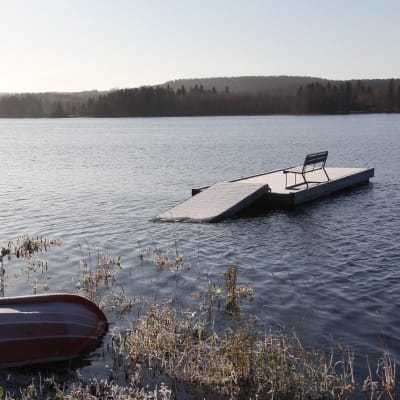 Vene rannassa Pielisen rannalla. Osittain veden alle jäänyt laituri, jolla penkki. 