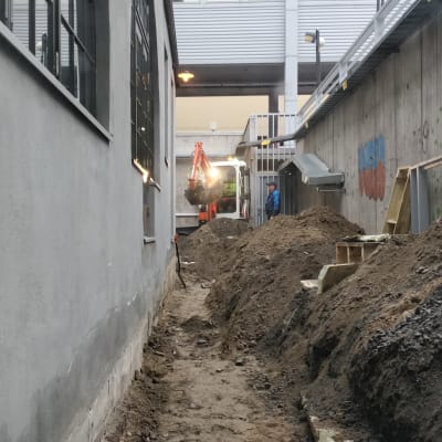 Kaivinkone työskentelee Valtiontalon seinän vierustalla ja kasaa maata pois seinän vierestä
