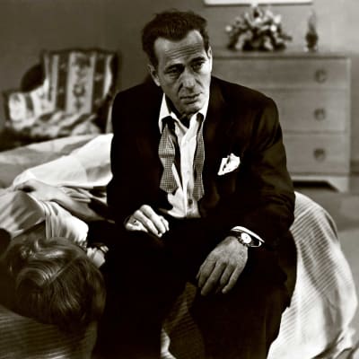 Huonovointisen näköinen mies (Humphrey Bogart) istuu paidan nappi ja solmuke auki sängyn laidalla. Kuva elokuvasta Hermot pinnalla (In a Lonely Place).