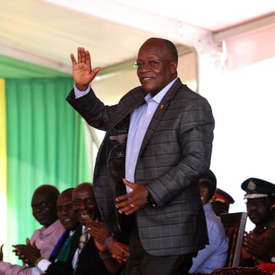 En äldre svart man i kostym står och vinkar med handen. Bakom honom sitter fler personer. John Magufuli inledde en ny presidentperiod i november 2020.