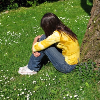 Ung kvinna sittande på gräsmatta.