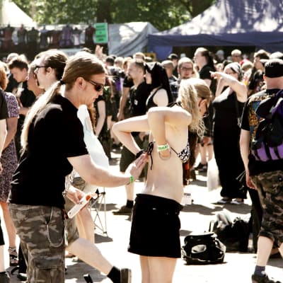 Man smörjer solkräm på kvinnas rygg på hårdrocksfestival.