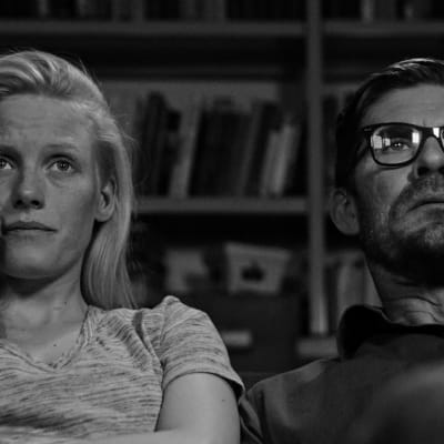 Närbild på Pihla (Laura Birn) och Eero (Tommi Korpela) som sitter bredvid varandra i soffan och ser på tv.