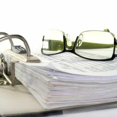 Ett par glasögon ligger på en hög med papper i en mapp.