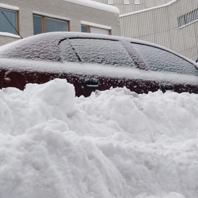 Tienvarteen pysäköity henkilöauto hautautuneena lumihankeen. 