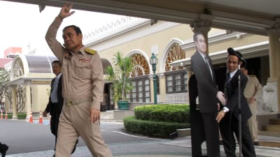 Prayuth Chan-ocha vinkar adjö efter att han placerat en kartongdocka framför journalisterna.