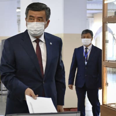 Sooronbai Jeenbekov pudottaa äänestyslipuketta vaaliuurnaan maski kasvoillaan
