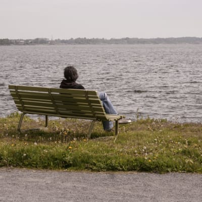Kvinna sitter på parkbänk och tittar ut över havet